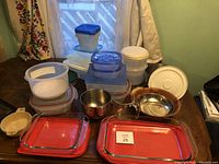 Overview of plastic containers, glass baking dishes with red lids, metal bowls, and measuring cup arranged on a table