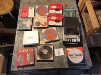 Top-down photo of a retro tape player with multiple vintage tape reels and their original boxes scattered on a table surface.