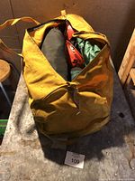 Photo showing large yellow bag containing camping and climbing gear including helmets and rolled items inside it.