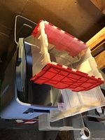 Multiple plastic storage bins stacked with translucent bin featuring red lid on top