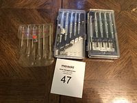 Three sets of small precision tools including screwdrivers and mini files in plastic holders and cases laid on wooden surface.