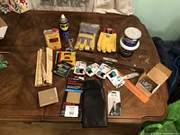Full view of tools and accessories on a table including wood putty, WD-40, gloves, hand cleaner, tool roll, sanding sheets, metal tools, screws.