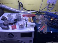 Photo shows wide assortment of tools and hardware laid out on a white surface including saw blades, screws, wiring, and fittings.