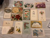 Photo showing full spread of 15 antique birthday postcards with floral, bird, and scenic designs on a table.