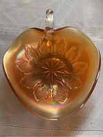 Top view: Marigold carnival glass bowl with single handle, embossed leaf pattern surrounding star base design, showing iridescent finish.