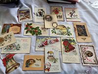Full display of 17 antique Christmas postcards arranged on a surface, showing varied designs including Santa Claus, holly, floral, cats, and winter scenes.