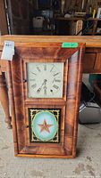 Front view of the antique ogee wall clock showing the clock face with Roman numerals and lower decorative glass panel with star design.