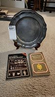 Antique wavy edged pewter plate displayed on wooden stand with two pewter collecting books in front.