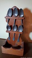 Photo showing six pewter spoons placed vertically in wooden display stand