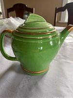 Side profile of the green teapot with visible gold trim on the handle, body, and spout showing the glossy finish.