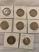 Photo showing eight Canadian 50 cent coins in white cardboard holders with handwritten dates and denominations. Coins appear in excellent condition.