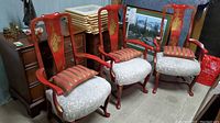 Full view showing all three vintage wooden Chinoiserie armchairs with red lacquer, gold painted designs, and upholstered seats with cushions.