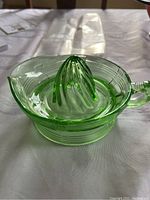 Photo of green Depression glass fruit juice reamer showing conical reaming center, handle, and spout on table.