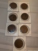 Seven English pennies dated from 1900 to 1907 in individual protective holders arranged on a table.