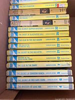 Box of fifteen Nancy Drew mystery books with visible yellow spines listing titles and edition years