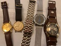 Photo showing five men's watches with different styles and bands on beige fabric background