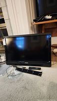 Philips 32 inch flatscreen TV on carpet with remote and wall mount bracket in front