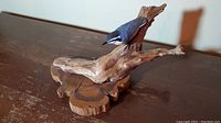 Side angle view of the bird carving perched on the natural wood branch base on a flat surface.