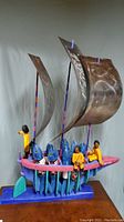 Full front view of entire painted wooden boat sculpture with metal sails, fish and fisherman figures.