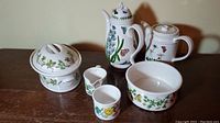 Full set showing coffee pot, teapot, creamer, sugar pot, bowl, and covered dish featuring botanical garden floral designs with butterflies.