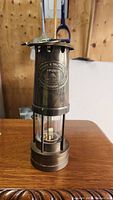 Front view of the brass Welsh miner's lamp showing the glass chimney and brass plaque on the body.