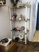Full view of one shelving unit with items displayed for scale (items not included in sale). The shelving unit is made of metal with brass accents and glass shelves, showing vintage wear.