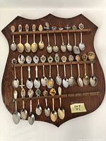 Photo showing 30 collectible spoons mounted on wooden display plaque arranged on three rails
