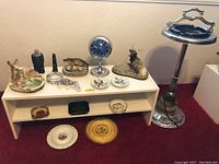 Wide view showing assorted ashtrays on white shelf, clock, animal figurines, and metal ashtray stand with black insert.
