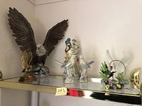 Shelf displaying four bird sculptures: large porcelain eagle, brass eagle on wood base, porcelain colorful birds figurine, and porcelain swan with flowers.