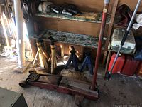 Photo showing vintage hydraulic floor jack in front of four car jack stands on a concrete floor in a workshop setting with some tools and shelves in background.