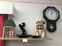 Wide shot of all items arranged on a shelf: musical cookie jar shaped like a hut, black horse ashtray, dog cookie jar, and Westclox Regulator clock on wall.