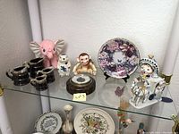Glass shelf display showing all collectible items including creamers, floral plate, and porcelain figurines.