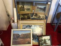 Overall assortment of framed paintings leaning against a wall and shelf showing frames and artworks in natural light.