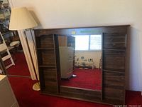 View of vintage wood headboard featuring shelf compartments and central mirror alongside tall floor lamp with pleated shade