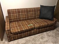 Front view of the vintage brown plaid fabric hideaway bed couch with black pillow on the right side.