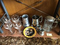 Photo showing all items in the lot including 4 Irish Coffee glasses, 2 pewter pint cups, 2 small pewter cups, a glass stein with pewter lid, and a round painted ashtray.