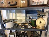 Overview photo of metal shelving unit with vintage kitchen items including scale, utensil trays, enamelware pot, rolling pin, spoons, and whisk