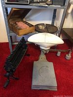 Wide view of vintage scale, paper roller, wooden liquor bottle set open box showing pink velvet covered bottle and shot glasses, and round tray on floor and shelf