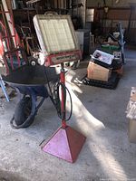 Side view of the vintage muffler service lamp with red triangular base, showing attached hose and surrounding workshop environment