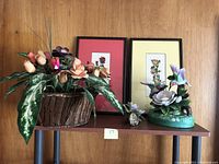 Overall view of two framed floral prints, porcelain musical flower arrangement in brown vase, faux flower arrangement on green base
