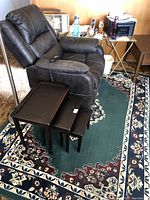 View of recliner chair with remote, nesting tables on rug, and part of a lamp base visible