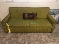 Front view of vintage green patterned Redi-Bed hideaway couch with one multicolor patchwork accent pillow on carpeted floor.