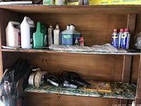 Shelf with multiple lubricant bottles including Spartan antifreeze, oil containers, and WD-40 spray cans on the top shelf, with assorted tools and clamps below.