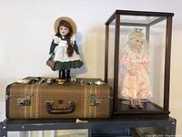 Wide view of vintage dolls, suitcase and glass display case with doll