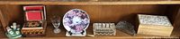 Wide shot showing all items in the lot arranged on a wooden shelf: wood boxes, collectible plate, glassware items including cut glass tray and basket, clear goblet, and figurines on a green ceramic dish.