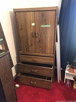 Front view of wooden dresser with three drawers at the bottom and double doors on top, partially opened to show interior storage.