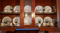 Full view of cabinet shelves showing the Royal Doulton Sarabande china set arranged along with clear and smoked stemware wine glasses.
