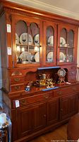 Front view of Pennsylvania House china cabinet filled with dishware and decorative items. Shows glass paneled upper doors and brass handles.