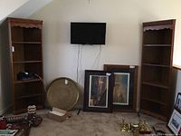 Pair of wooden corner cabinets placed against wall with items around them. Cabinets have scalloped edges along the top and five shelves each.
