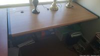 Top view of laminate desk showing light wood grain finish and black trim edges with scratches and water marks visible on surface. Desk supports various lamps and small decorative objects, contents not included.